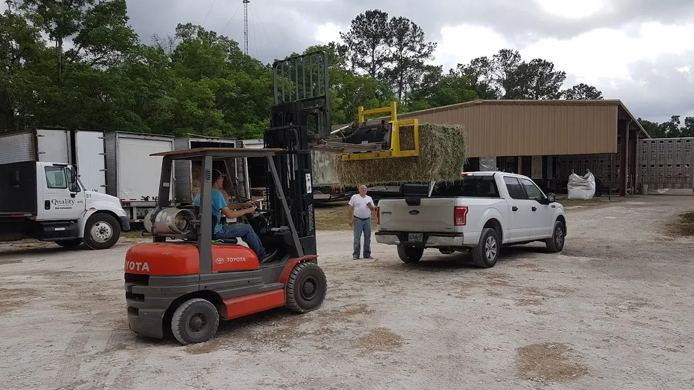 Team loading hay bales onto customer truck with forklift